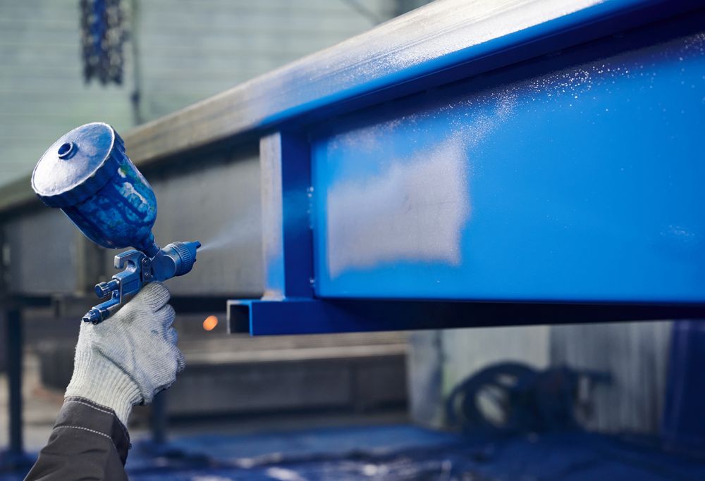 A person sprays blue paint on metal. 