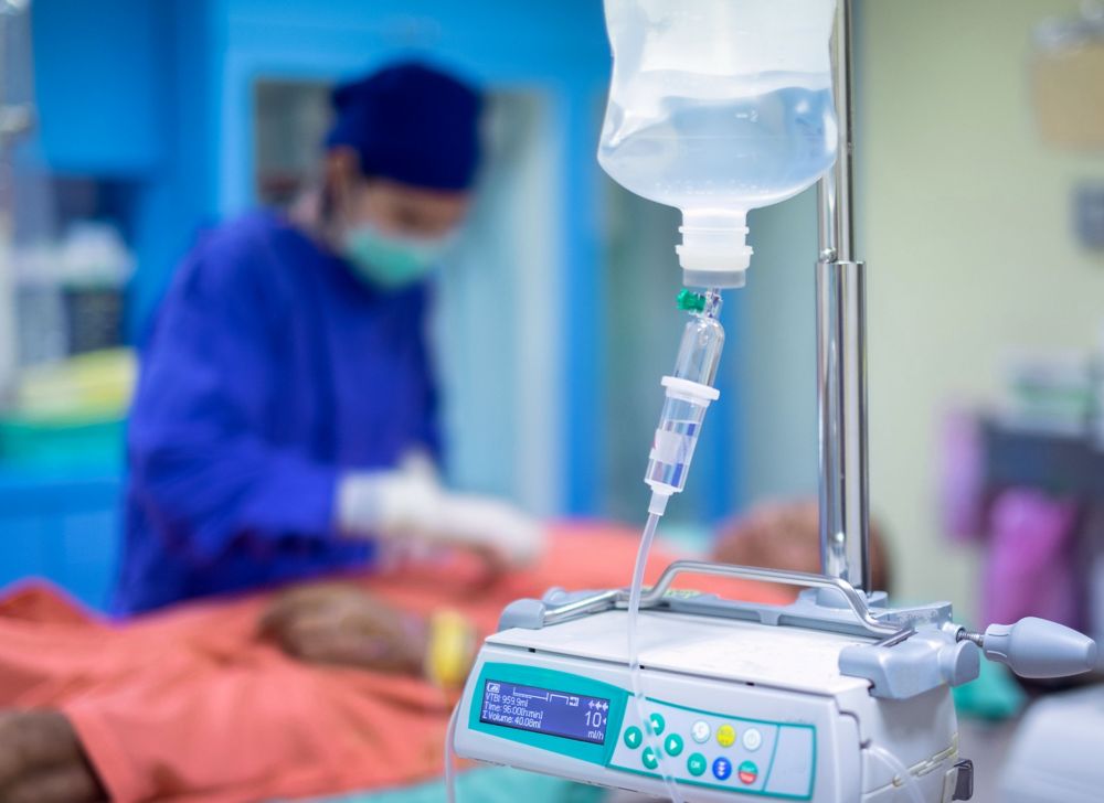 A close-up of an IV bag in front of doctor checking on a patient. 