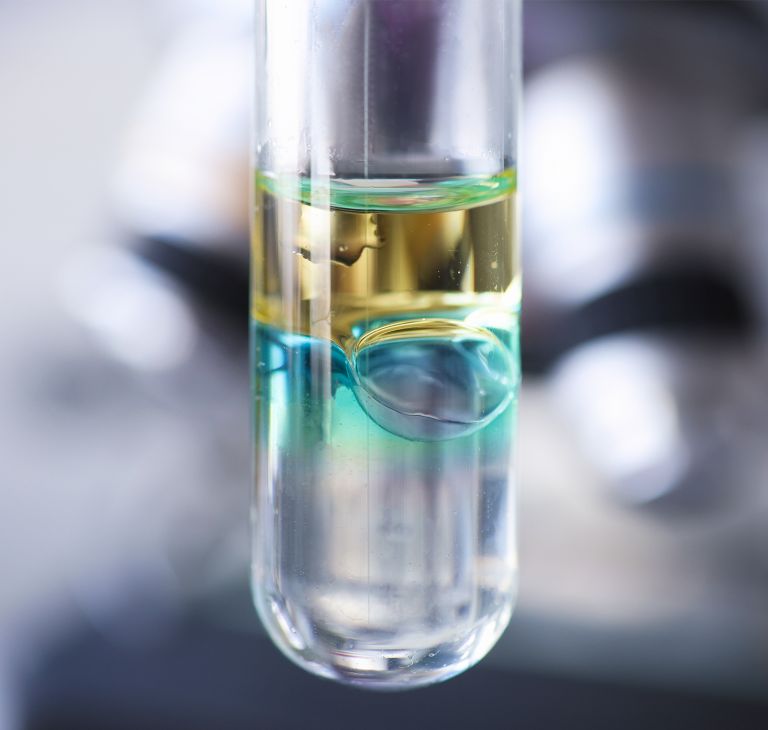 A close-up of a test tube with layered yellow, blue and clear liquids. 