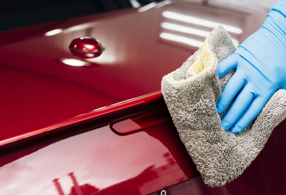 A person wipes clean a red car using a cloth. 