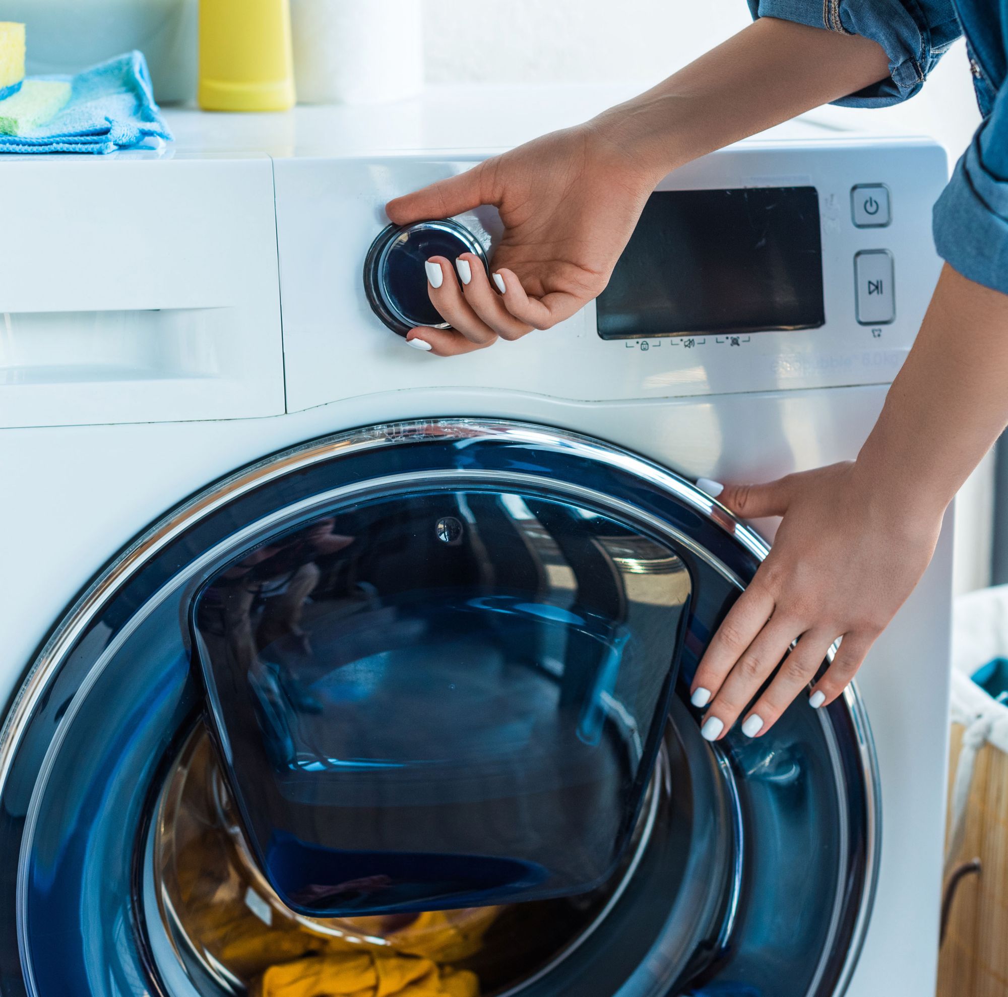 A closeup of a person starting a washing machine filled with clothes. 