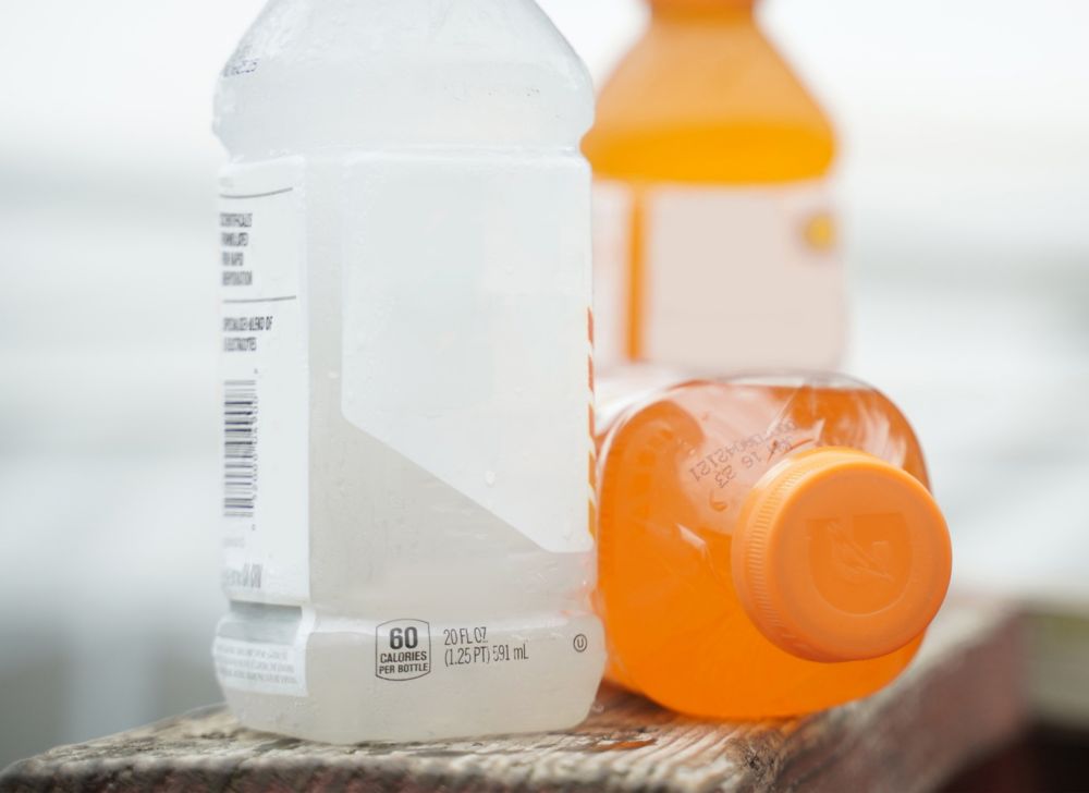 A close up of a white electrolyte drink next to an orange electrolyte bottle laid down on its side 