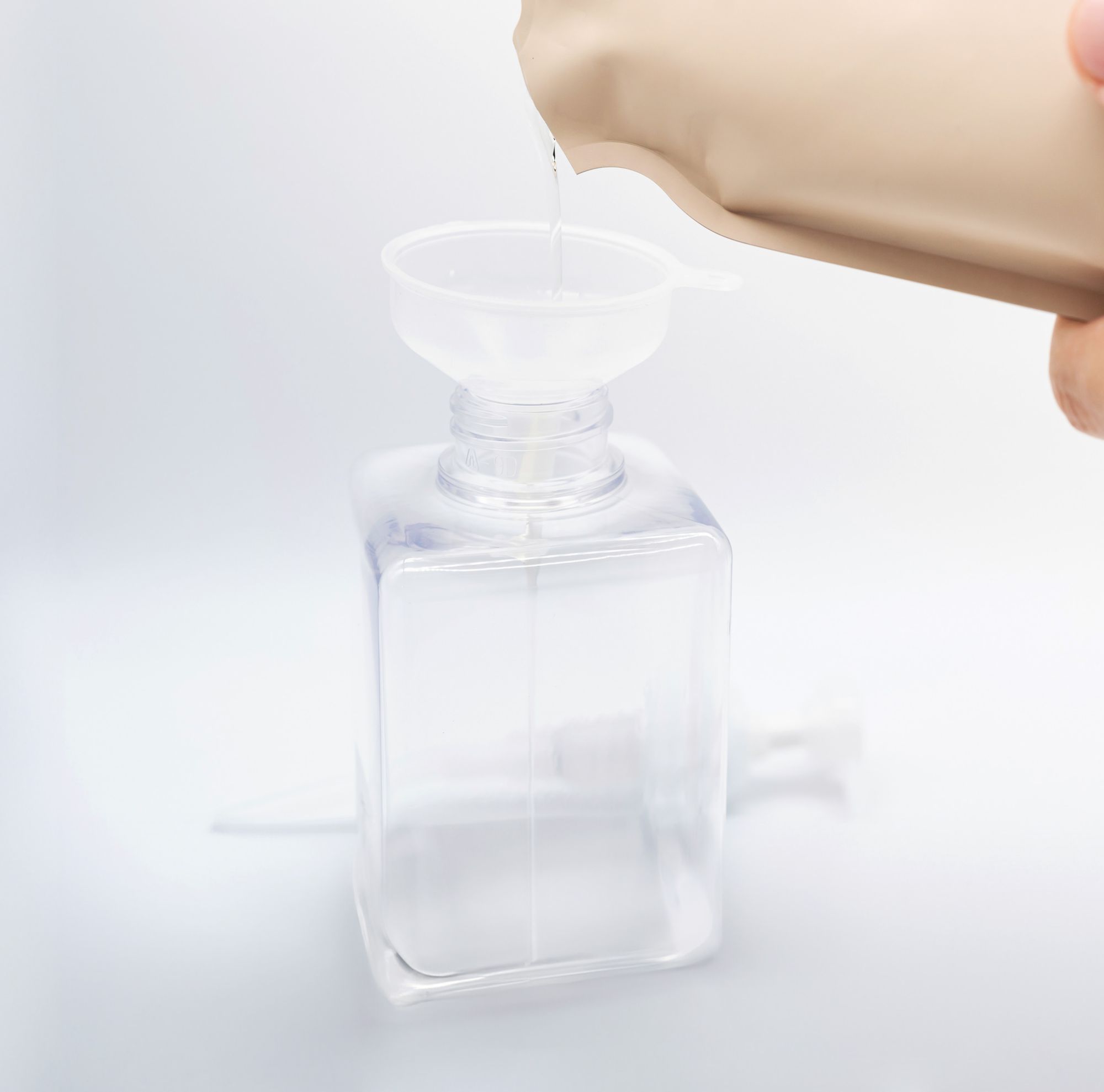 A person pouring refill liquid into a clear, reusable cosmetic bottle. 