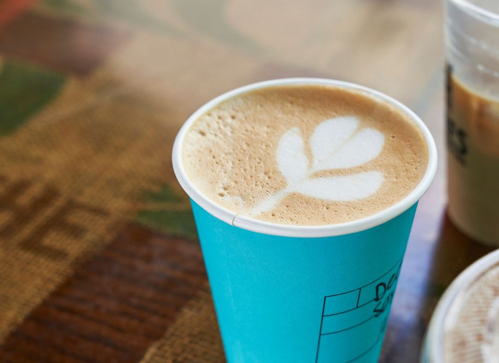 A flower latte in a blue paper cup.  