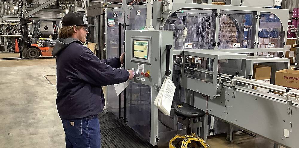 A man presses a button on a large piece of machinery in a workshop. 