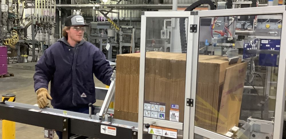 A man feeds cardboard boxes through a large piece of machinery in a workshop. 