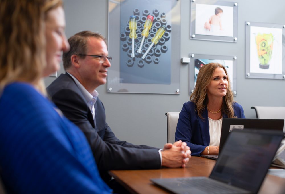 Three people meet in a conference room with laptop computers. 