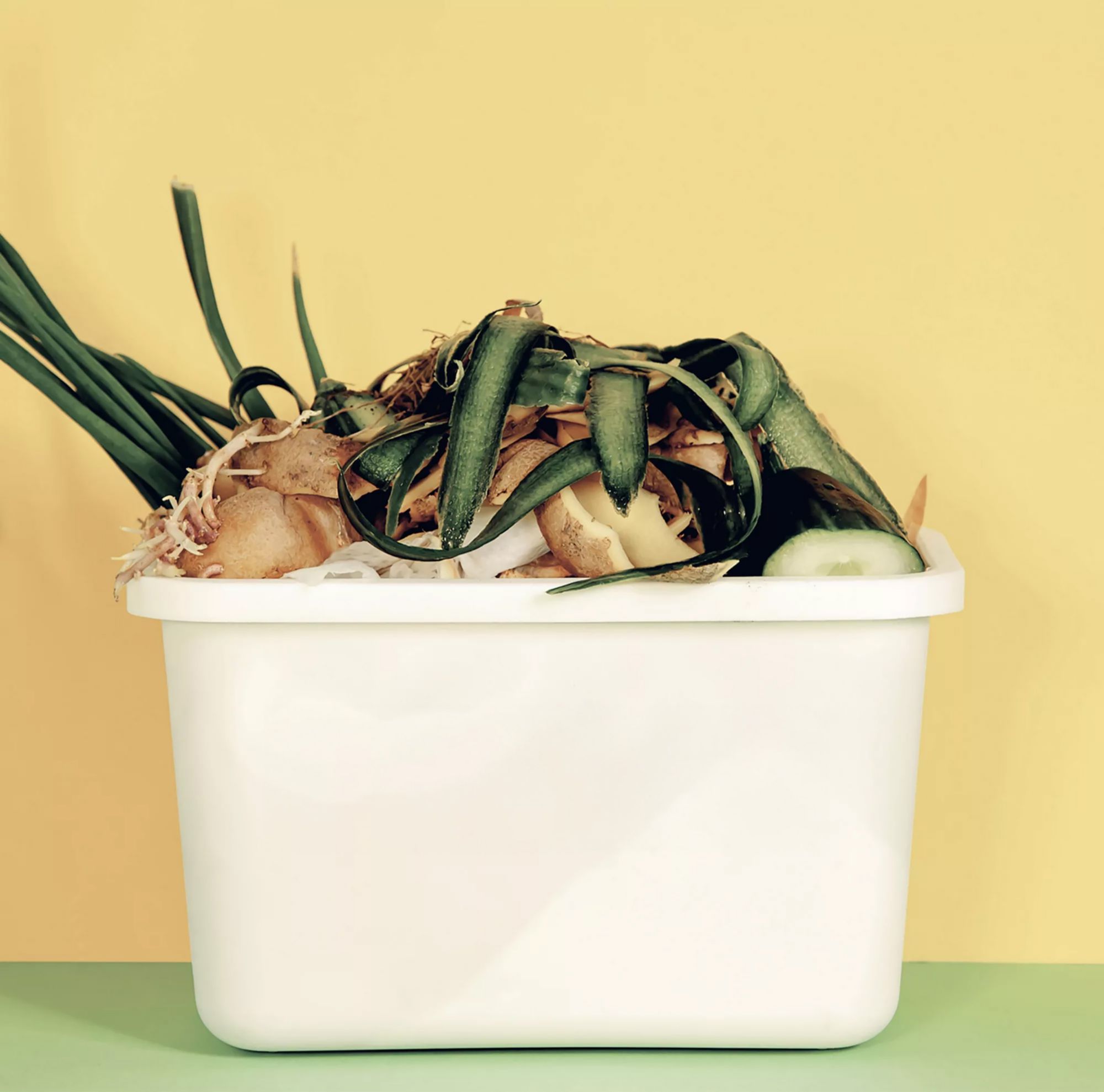 A white compost bucket overflowing with vegetable scraps. 