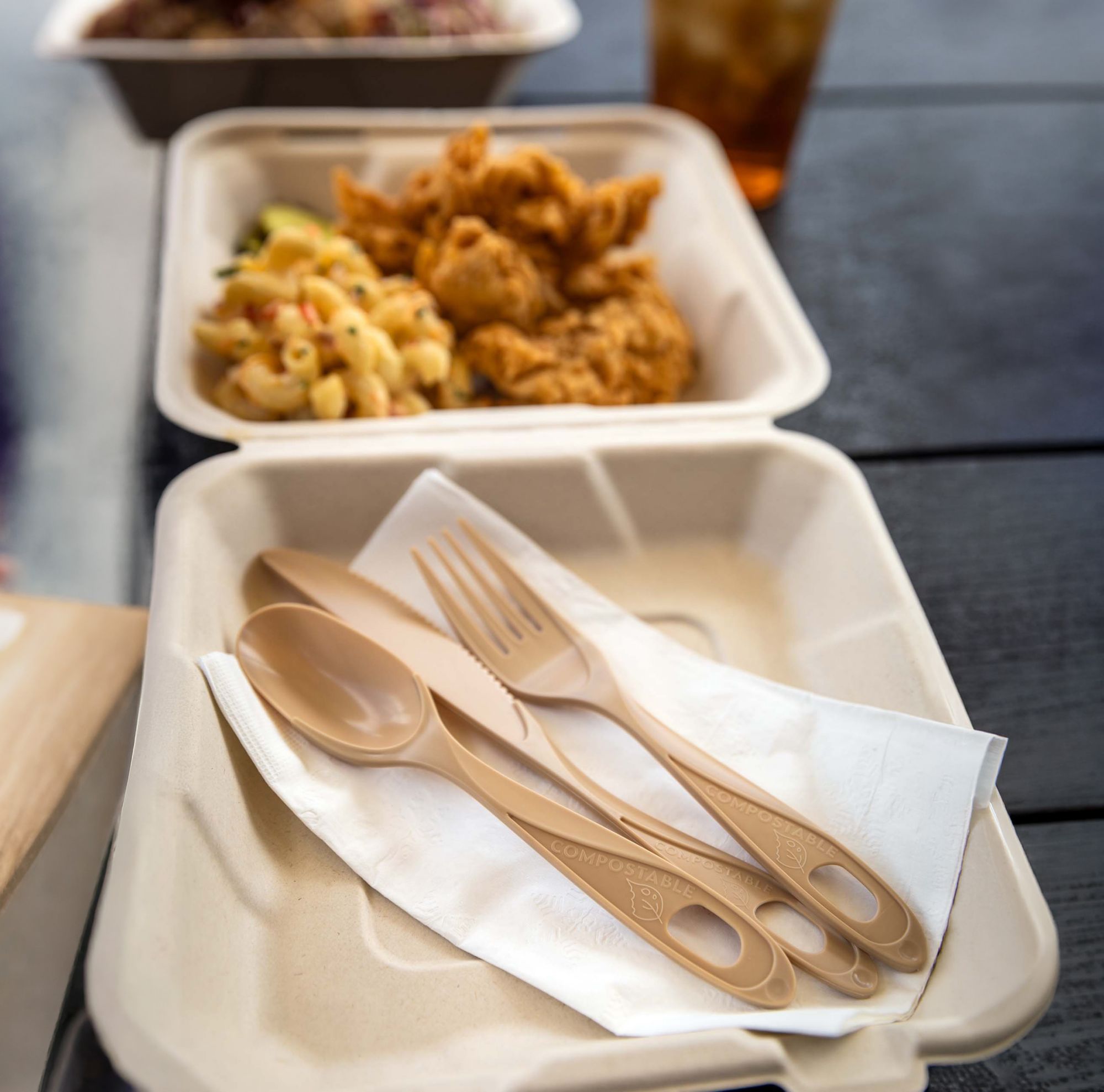 Compostable spoon, fork and knife placed inside a takeout box of fried chicken. 