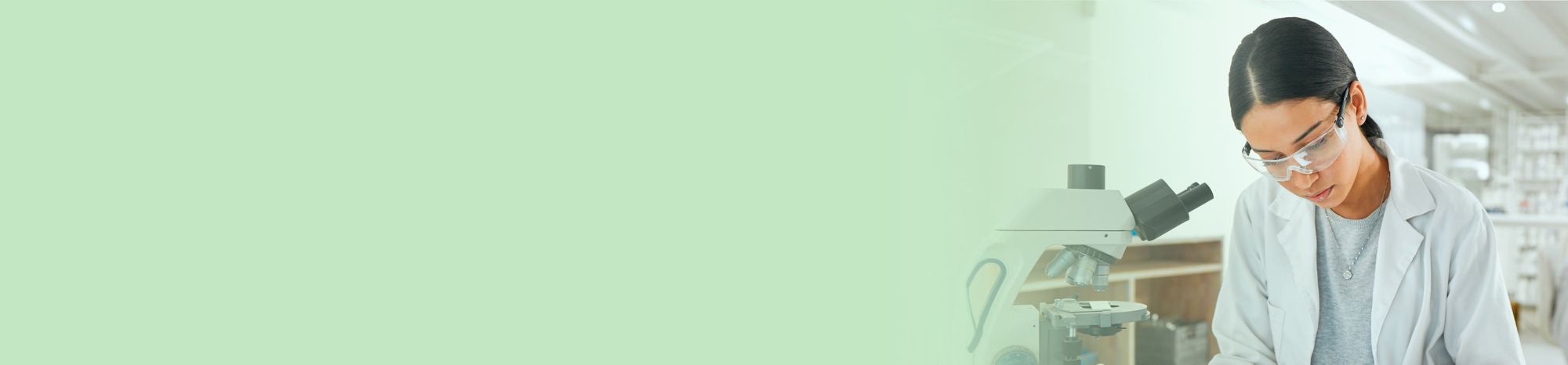 A scientist is jotting down observations beside a microscope 