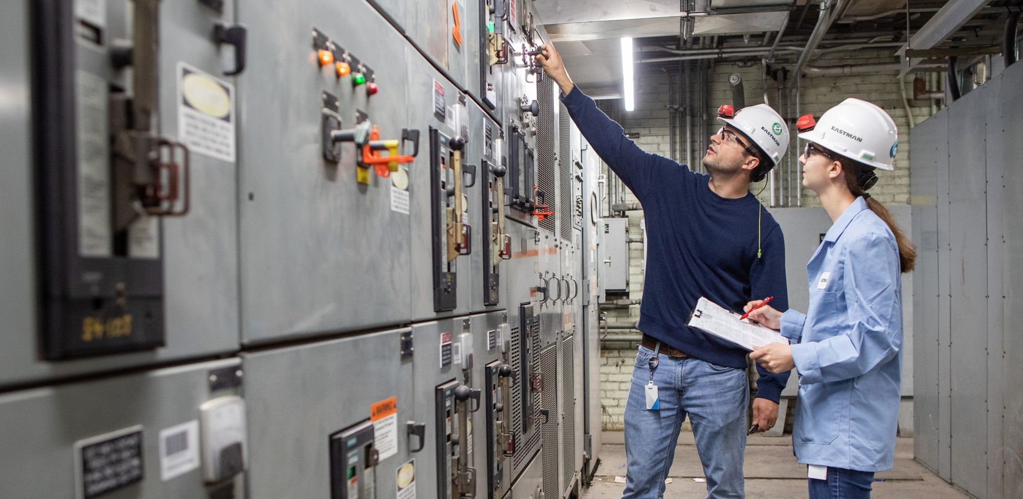 Dos empleados con EPP y parados fuera de una planta de Eastman hablando entre sí. 
