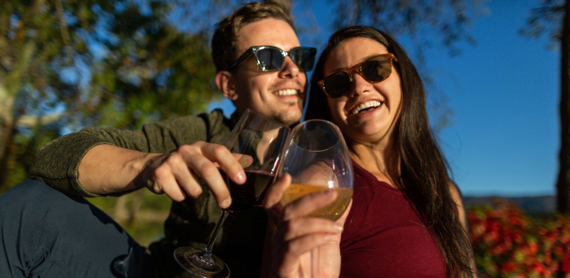 A smiling couple wearing sunglasses and holding wine glasses. 