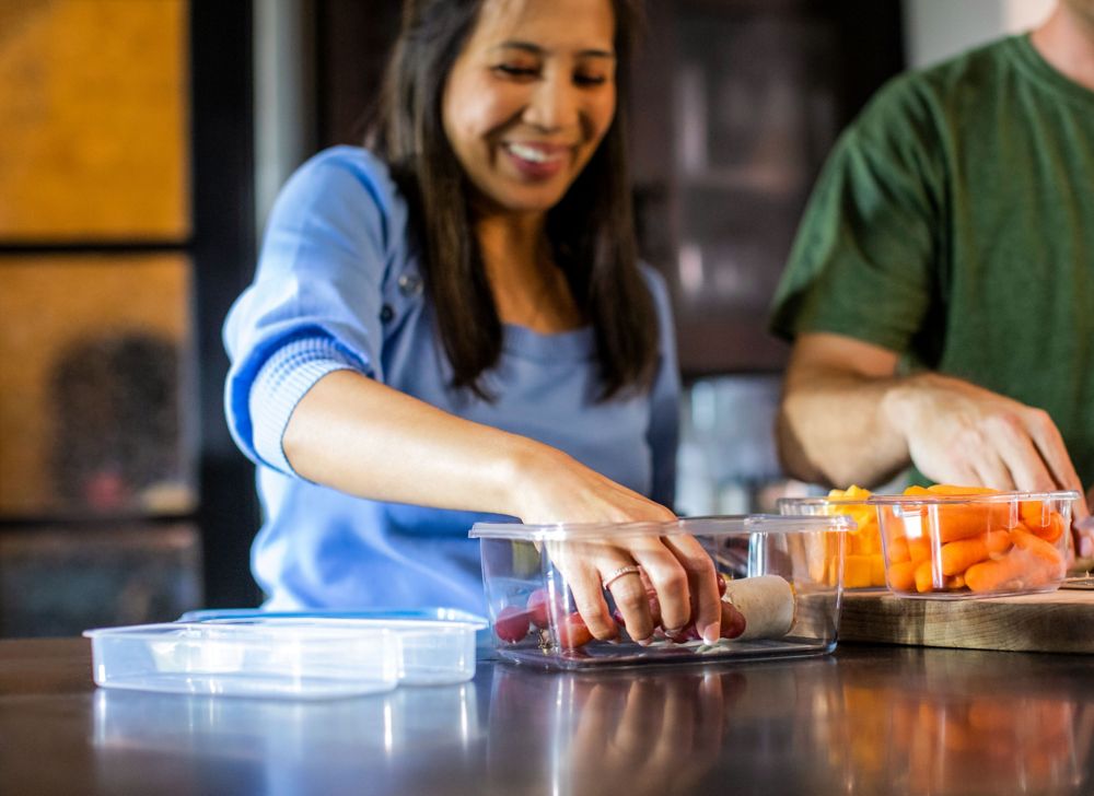 A woman grabs food from a small, clear storage container. 