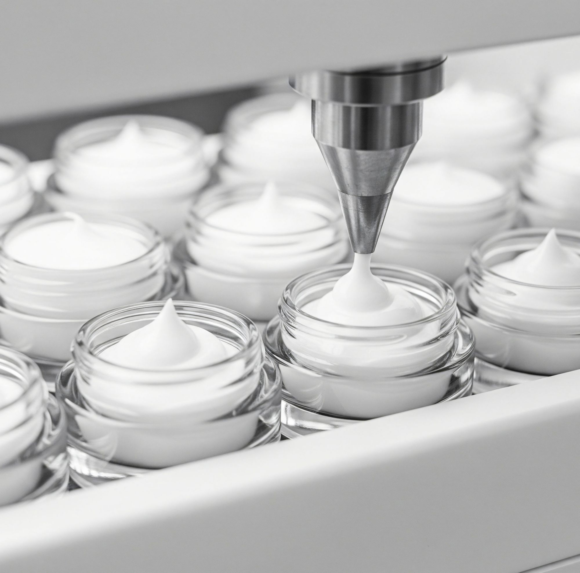 Clear cosmetic jars on a conveyor belt being filled with face cream.  