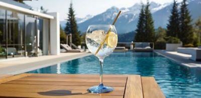 A long-stemmed gin tonic glass by HappyGlass rests beside a pool.   