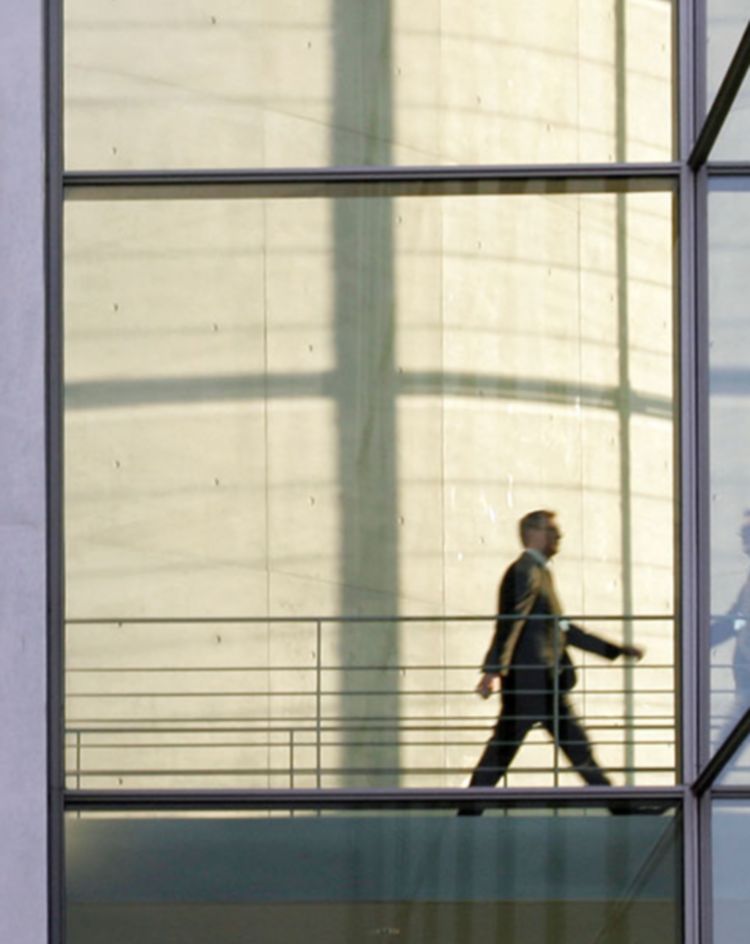 Glass‑walled building interior with a person walking across a skybridge. 