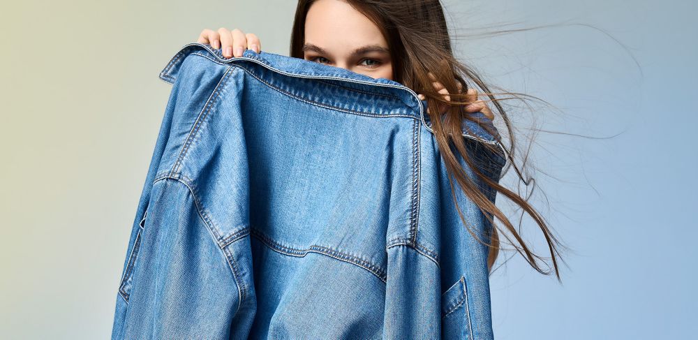 A person holds a denim jacket up to their face. 