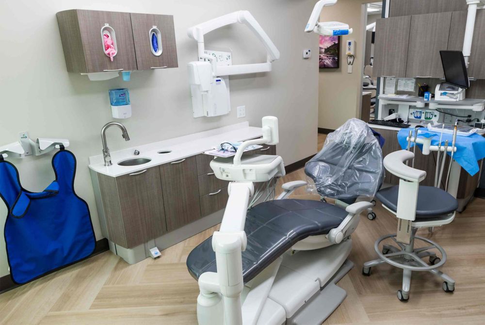  A dental chair is surrounded by various equipment and computers in a bright room.  