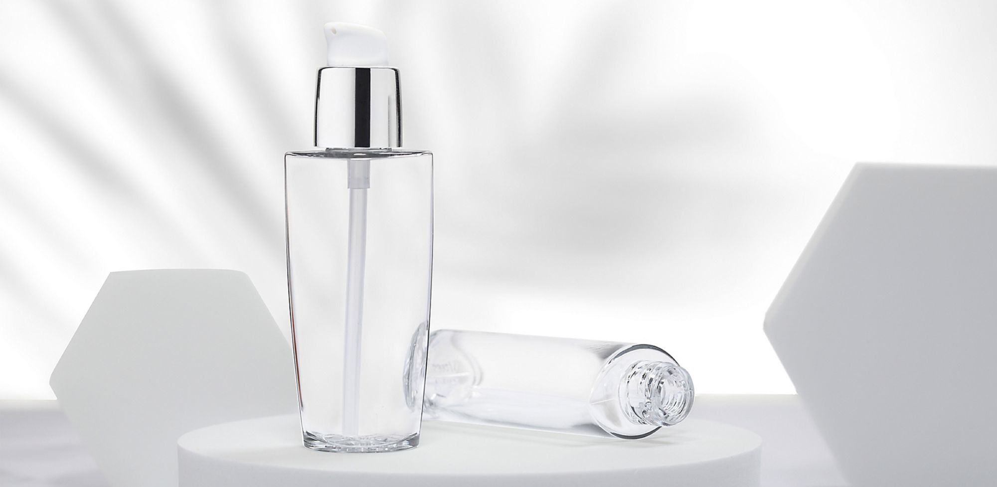 Two clear cosmetic bottles on a white pedestal. 