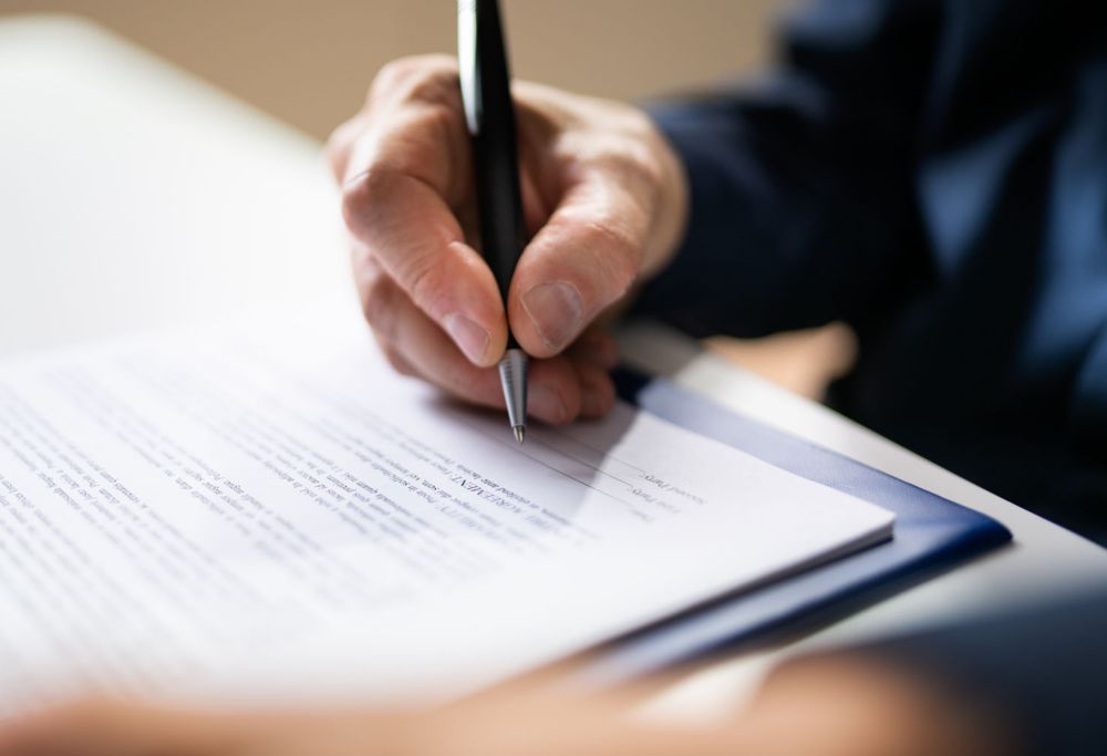 A close-up of a person holding a pen and ready to sign a document 