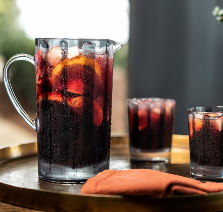 A pitcher and two cups filled with a dark-colored drink. 