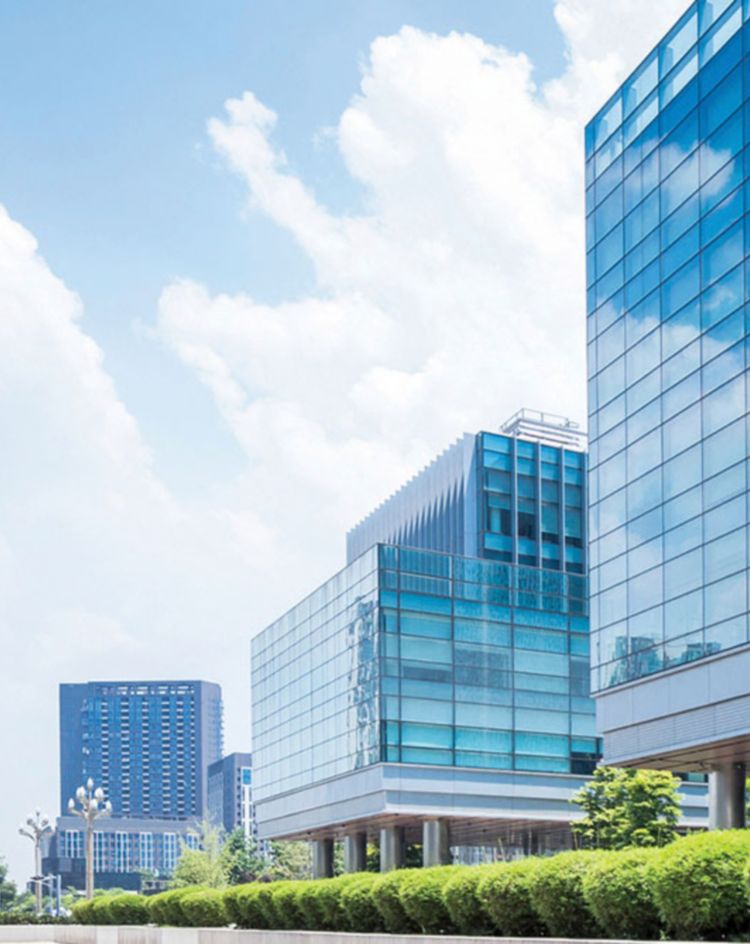 Glass‑clad office complex with trees and shrubs along the walkway. 