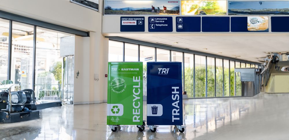An Eastman-branded recycling bin and a trash bin are located inside the airport.  