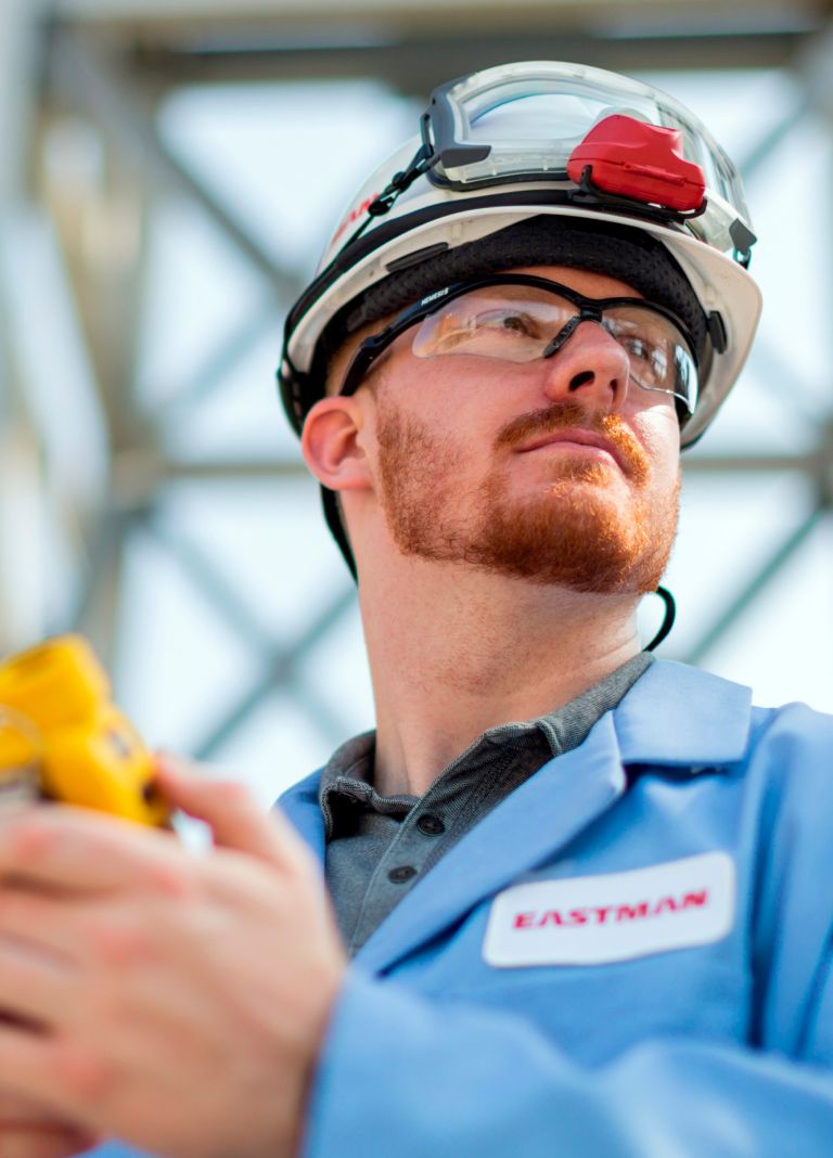 An Eastman worker in proper protective equipment holds a measuring device. 