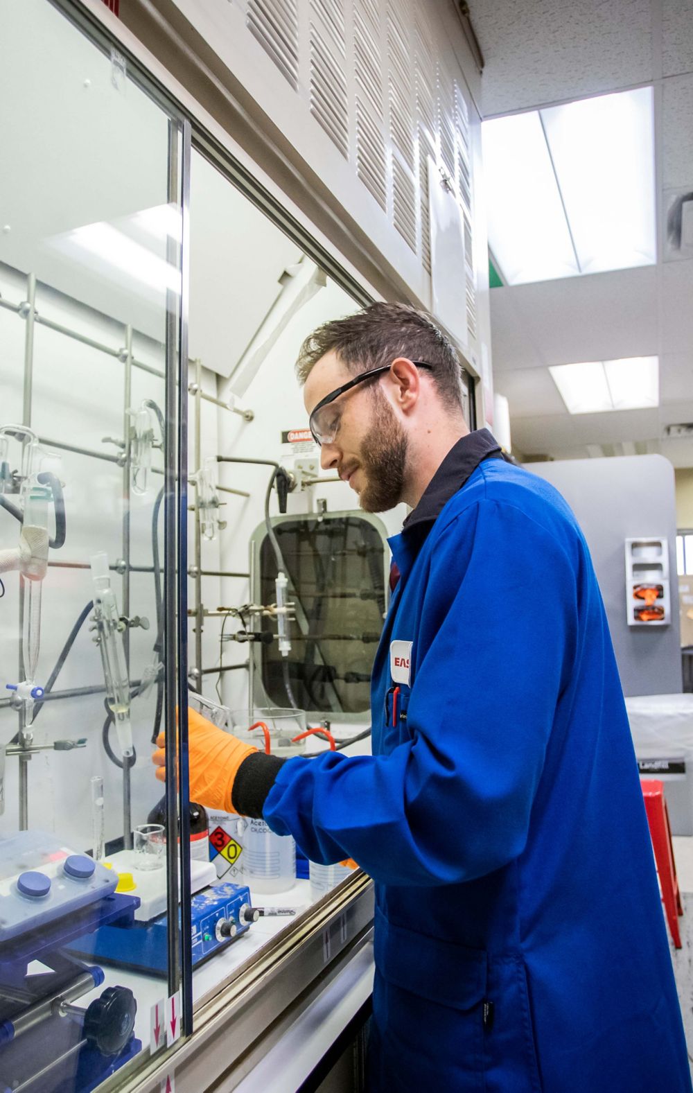 Engineer in a blue lab coat working with glassware. 