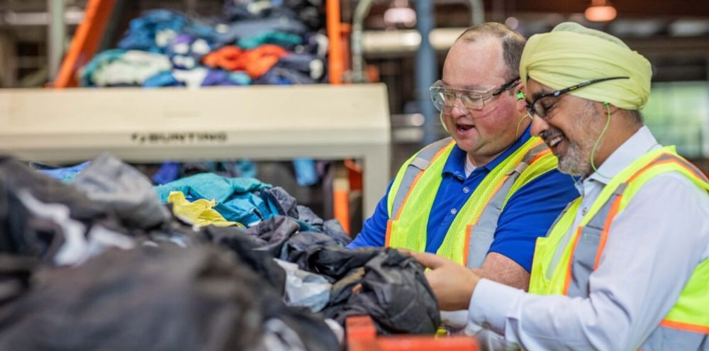 Two people in protective gear sort discarded textiles for recycling. 