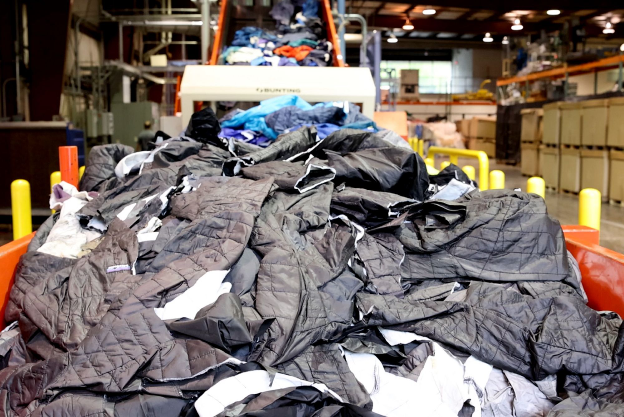 A large pile of waste apparel is loaded onto a conveyor. 