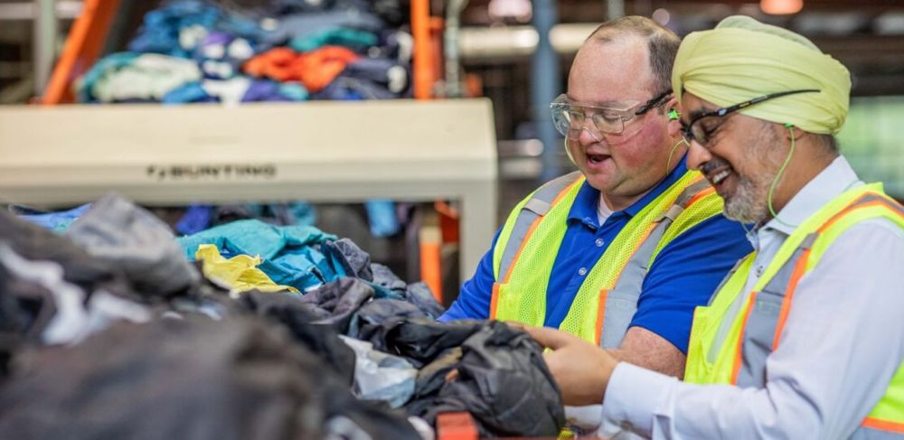 Two people in protective gear sort discarded textiles for recycling. 