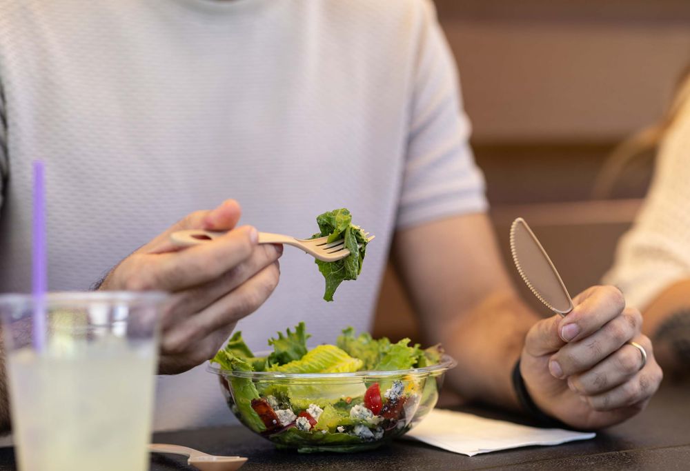 A person eats a salad with a compostable fork and knife. 