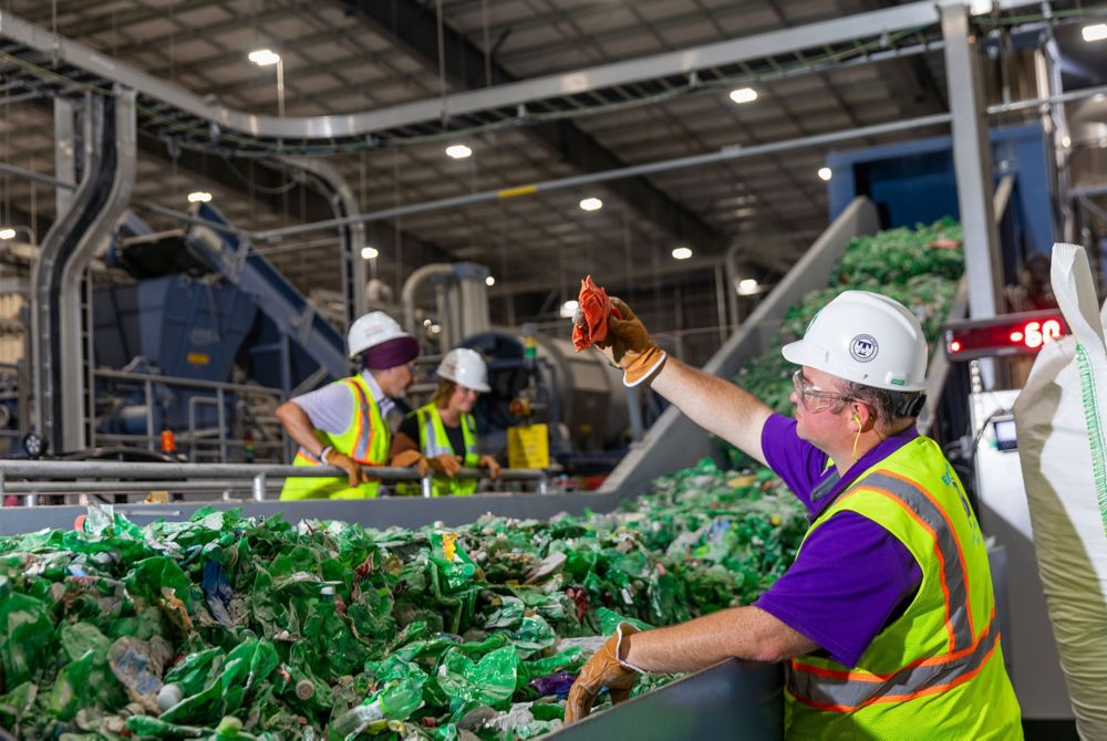  Eastman workers in safety vests examine waste plastic items on a conveyor belt.  