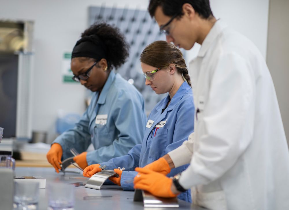 Three PPE-wearing scientists working side by side on a lab bench. 