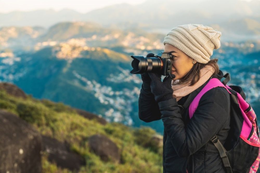 Woman taking a picture with an analog camera from the top of a mountain 