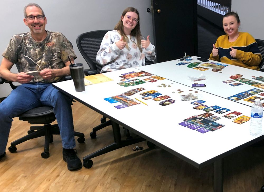 Three Eastman employees smiling at the camera next to their board game. 