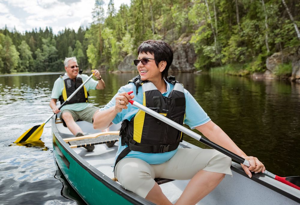 A couple wearing life jackets canoeing in a lake surrounded by trees. 