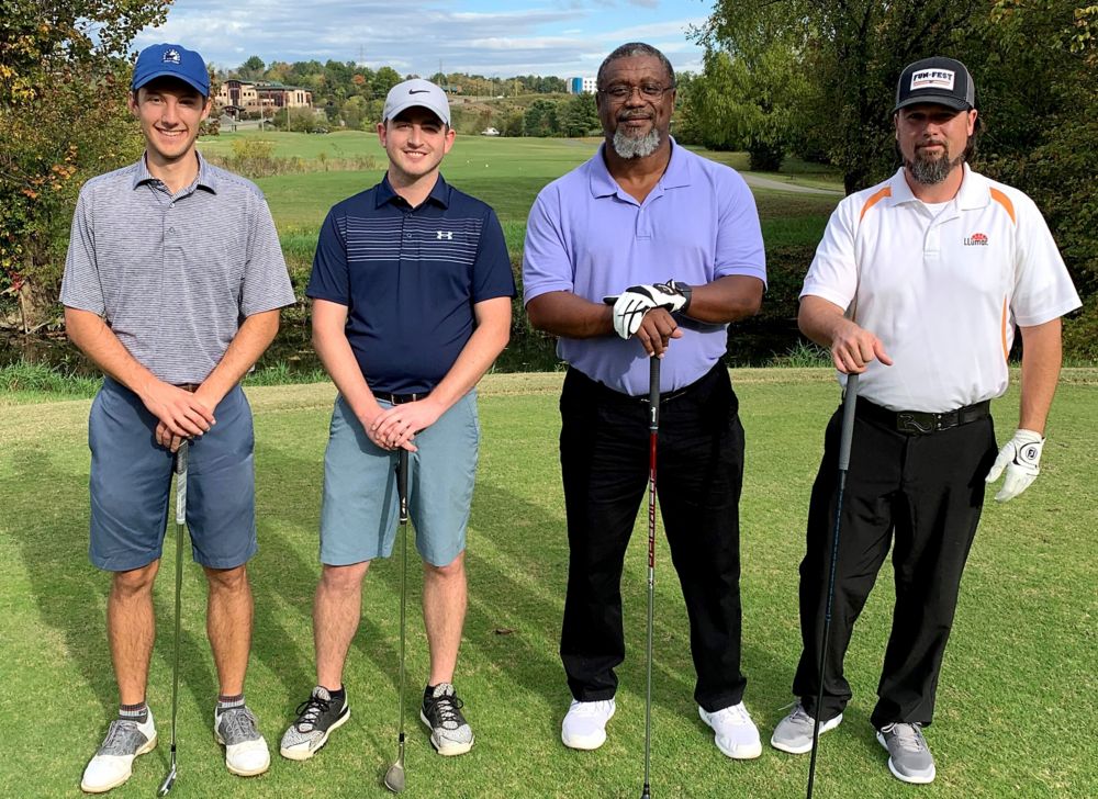 Four Eastman golfers holding their clubs and smiling on the golf course. 