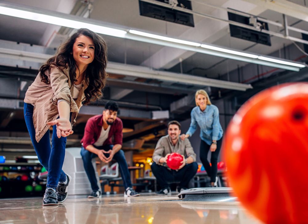 A person throwing bowling ball as friends watch. 