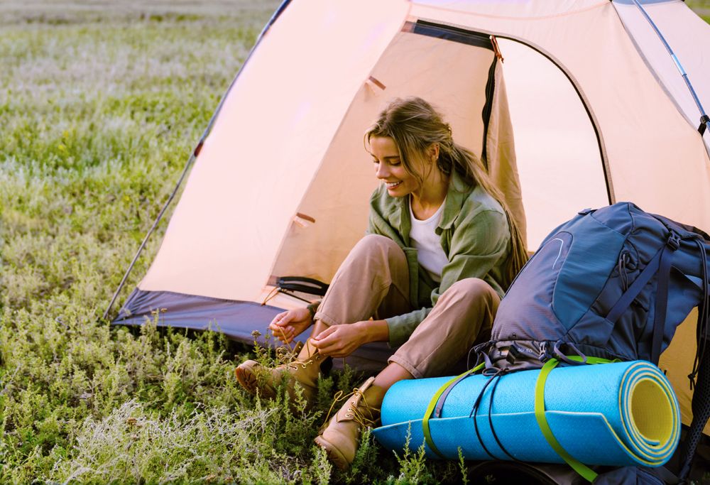 A woman tying her boot laces by a tent. 