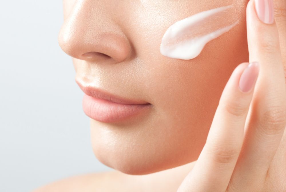 A person applies cosmetic cream to their cheek with their fingers. 