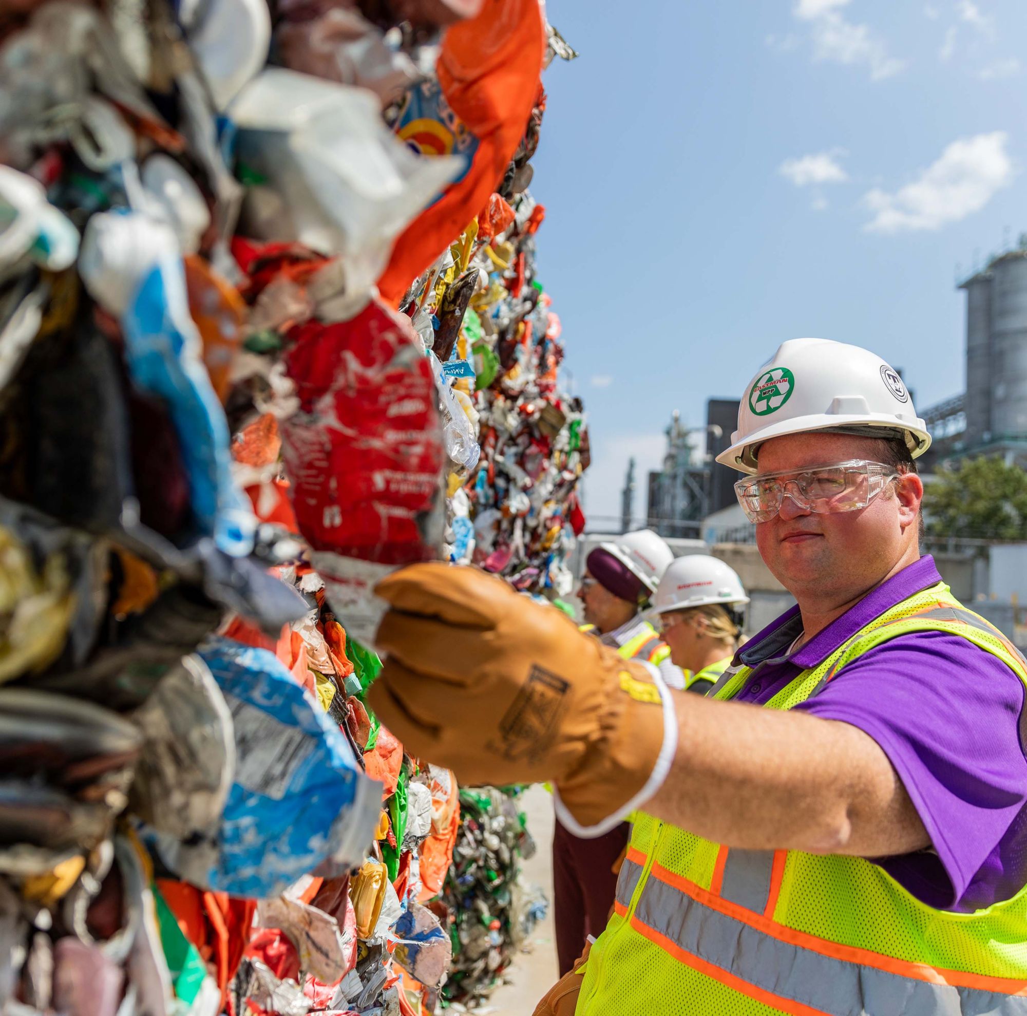 Workers inspecting compacted plastic bales at a recycling plant. 