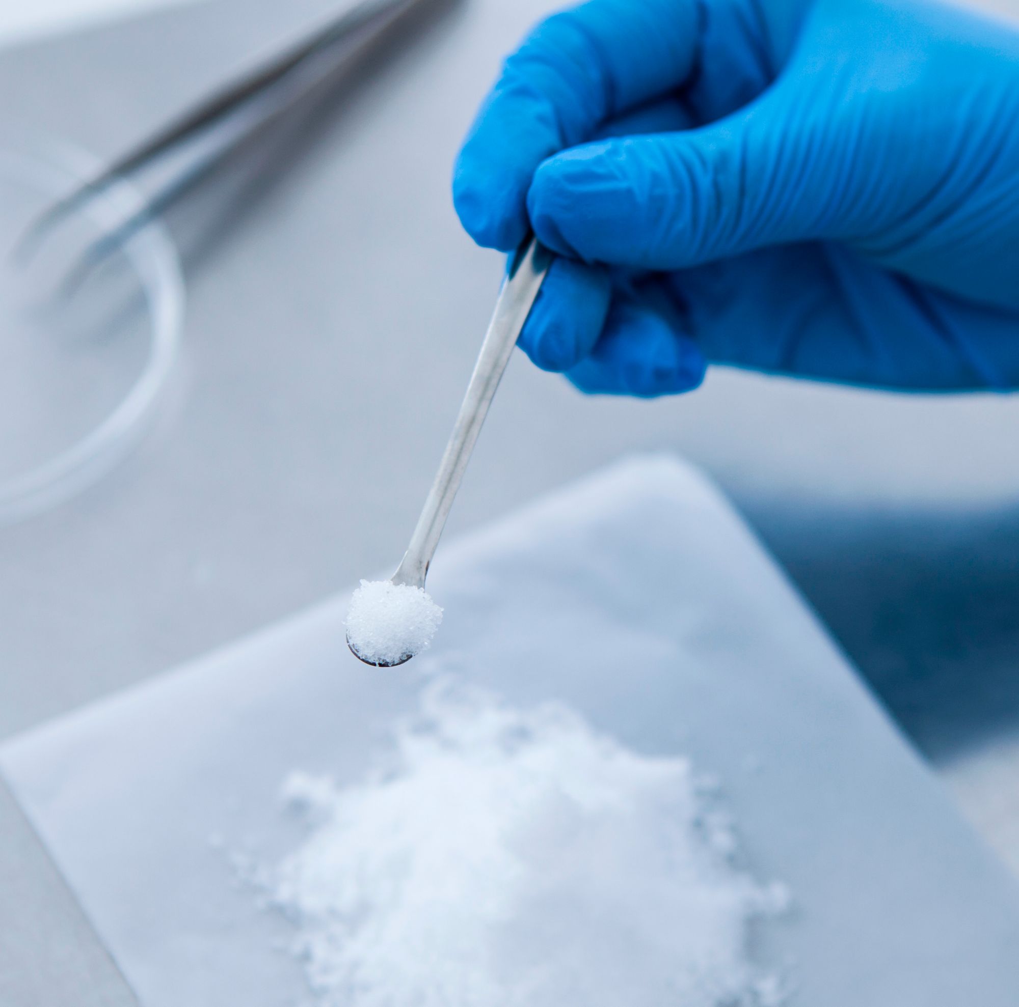 A scientist holds a small scoop with white powder 