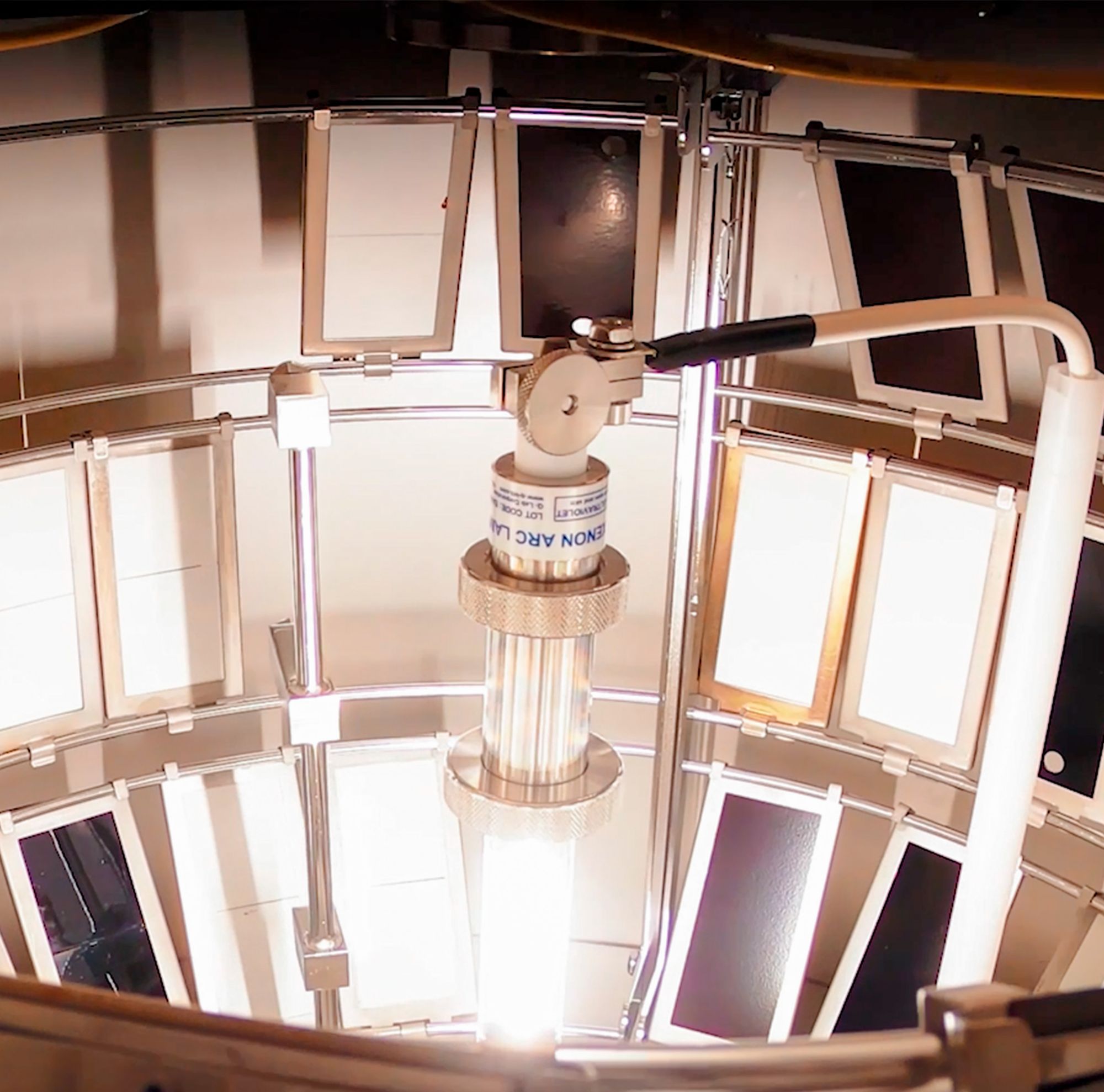 A weathering testing device with a central light source surrounded by various plastic sheets. 