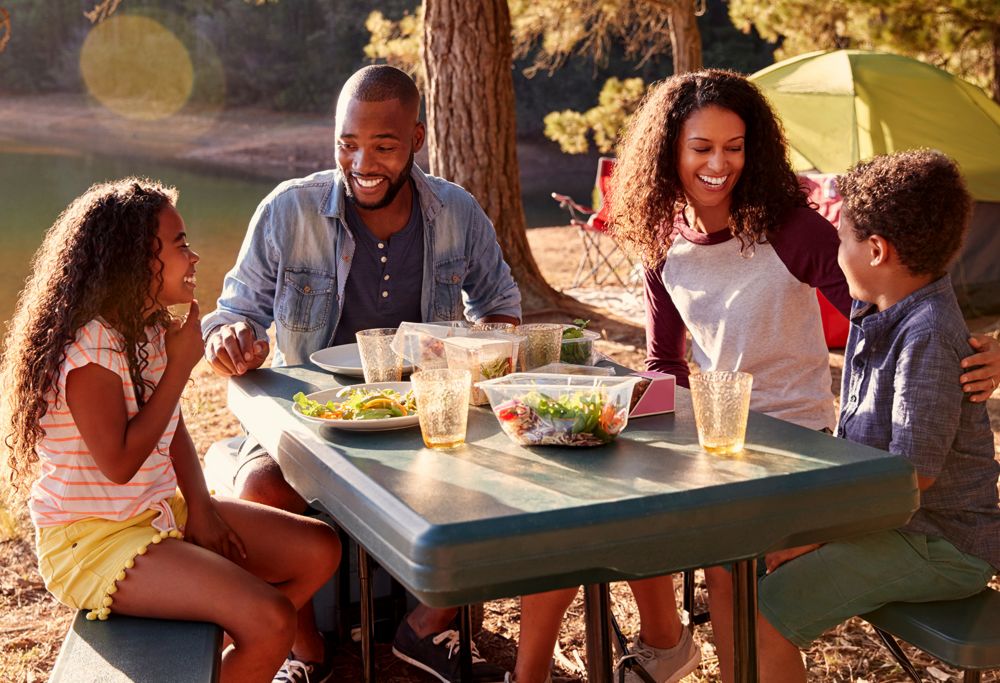 A family with two small children eats dinner at their campsite. 