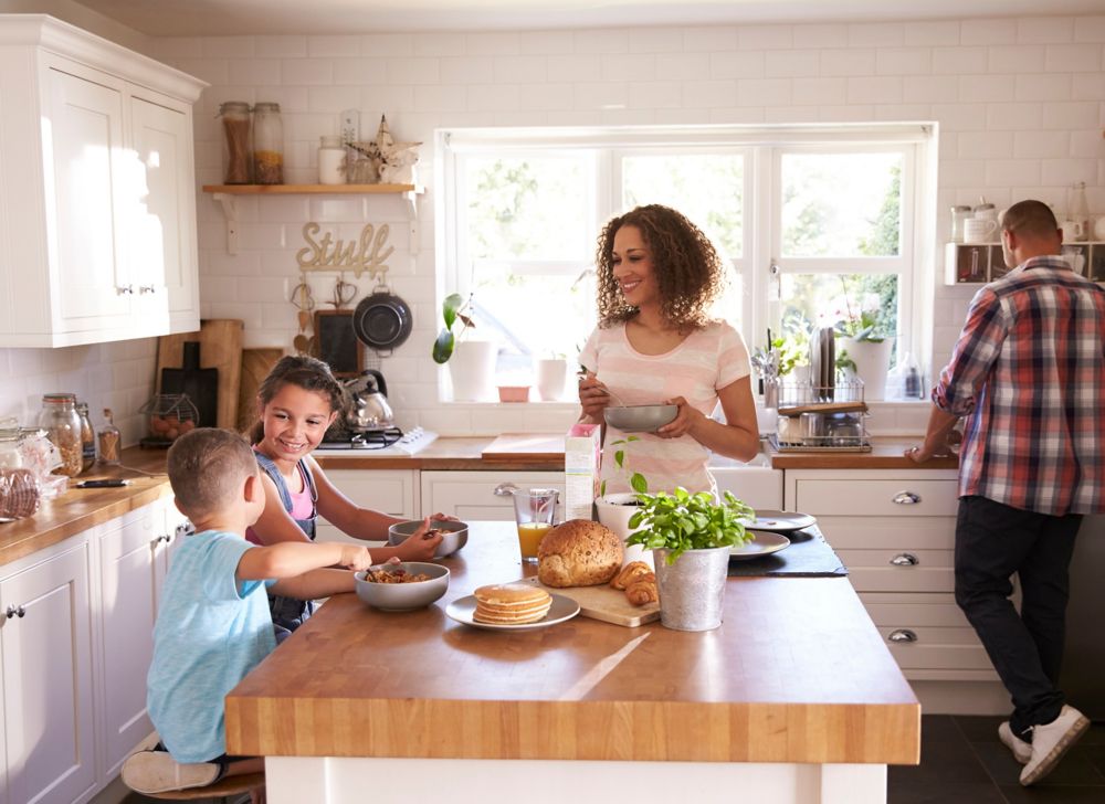 A man and woman are in the kitchen where two children are eating. 