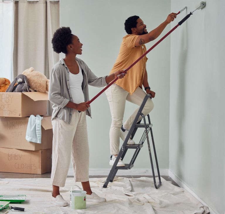 Two people paint walls with a roller brush and hand brush. 