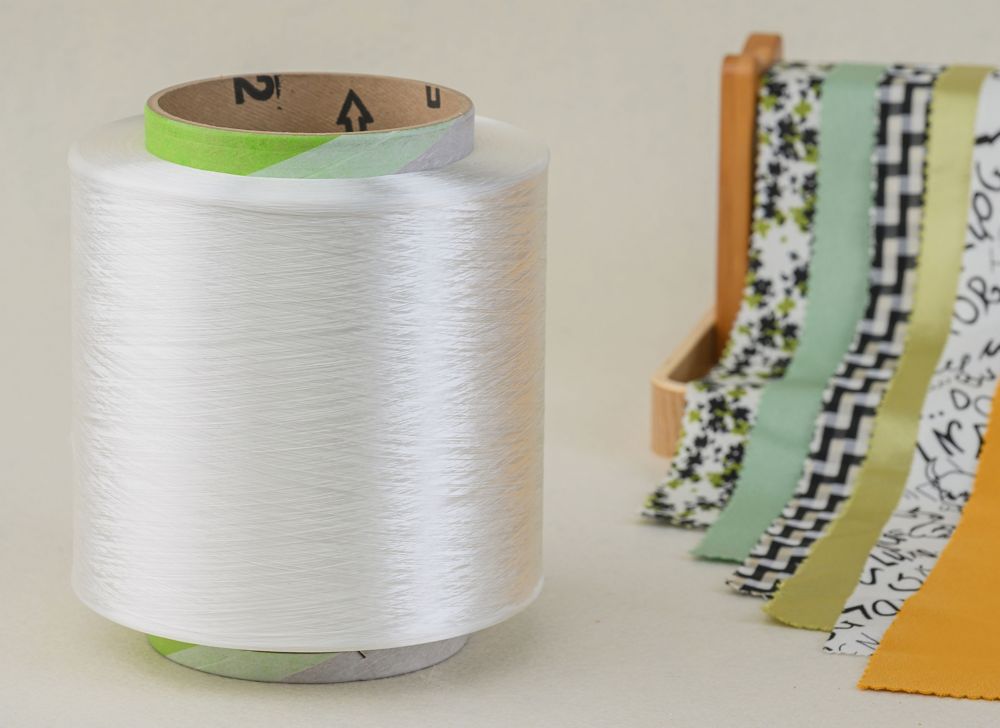 A spool of Naia™ filament yarn sits beside multicolored fabric. 