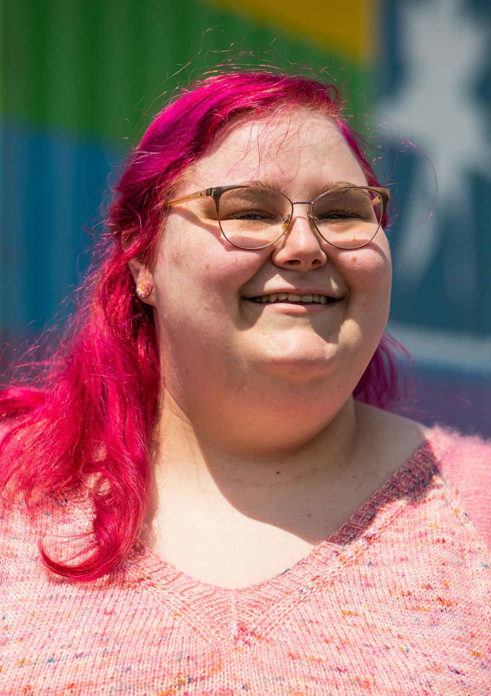 A close-up of lab technician Elaina Campbell smiling in front of a rainbow-color trailer 